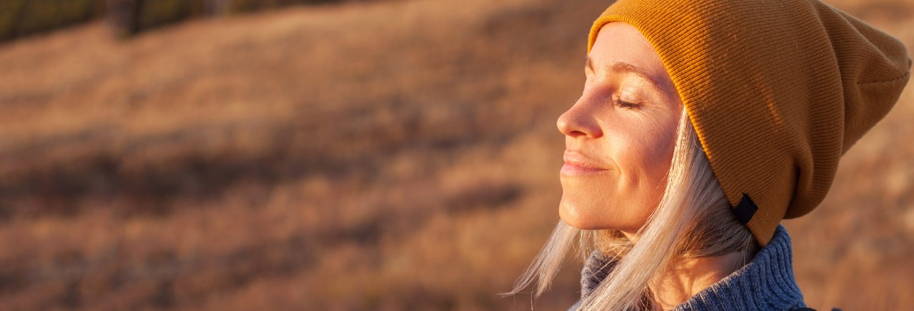 Kvinna står på ett fält med stängda ögon och solen i ansiktet.