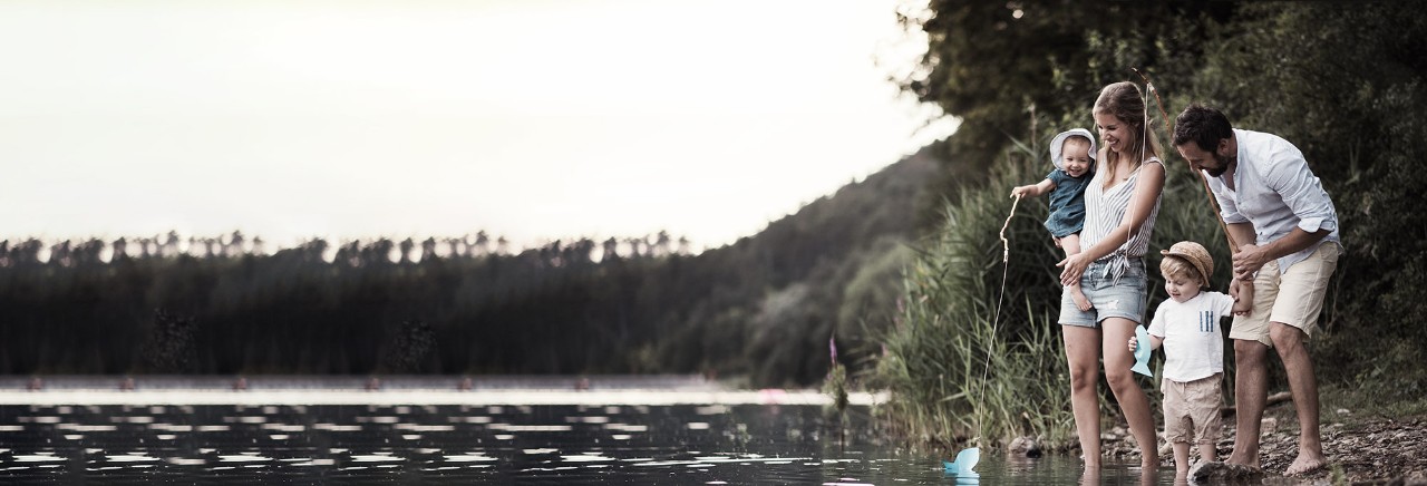 En ung familj med två småbarn utomhus vid floden på sommaren.
