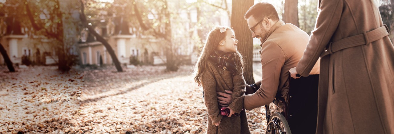 Pappa i rullstol njuter med sin dotter och fru utomhus under hösten i parken.